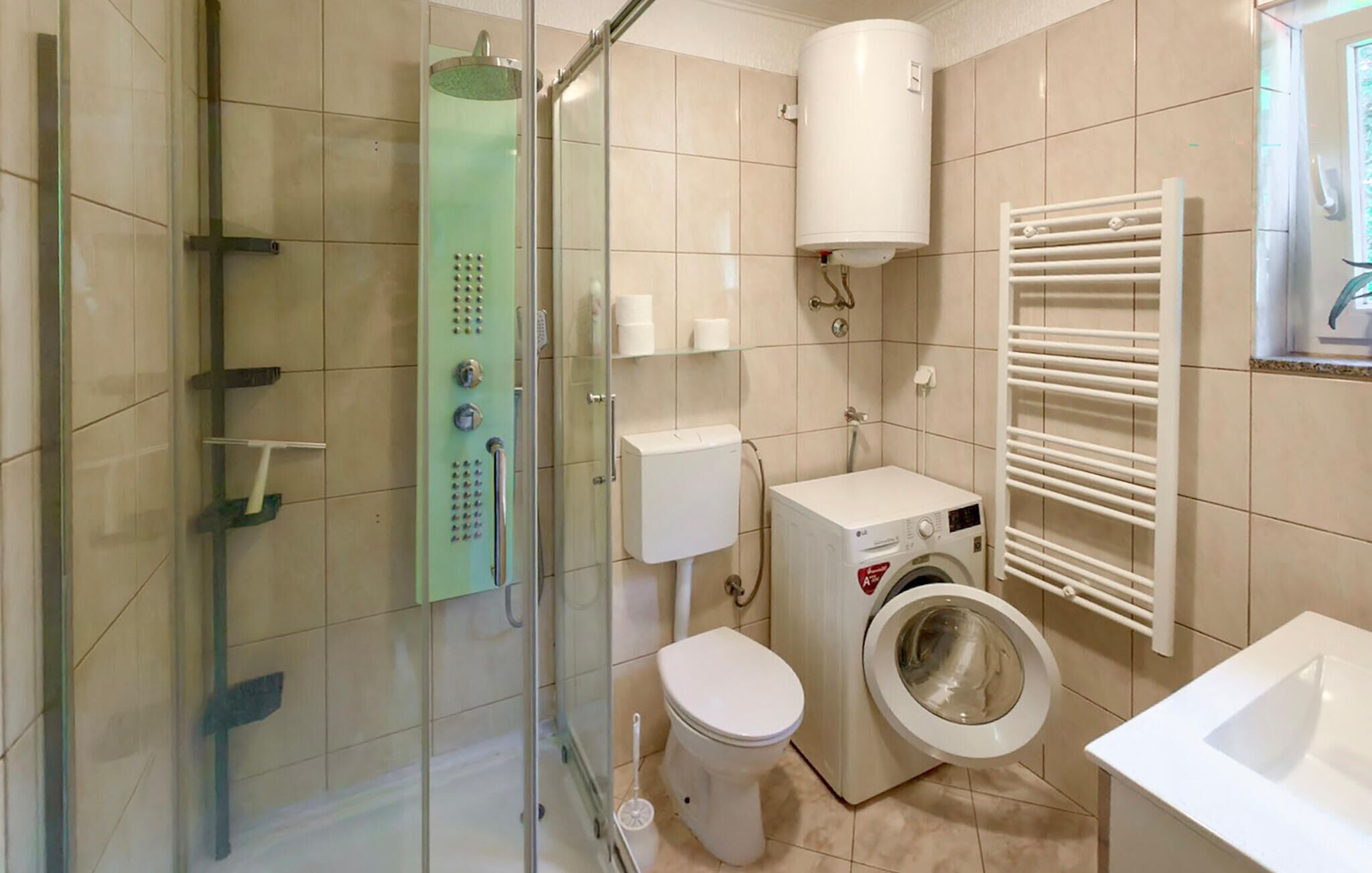 A bathroom with a glass shower enclosure, a toilet, a washing machine, and a towel rack.
