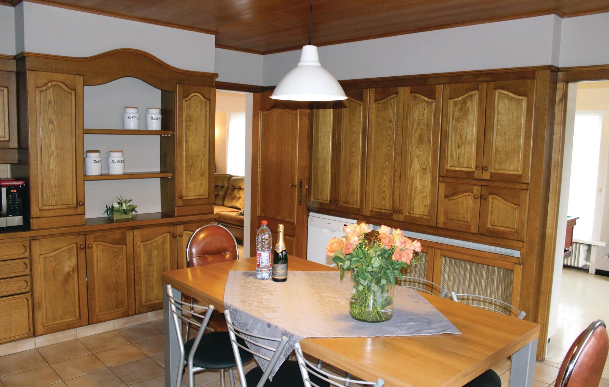 Eine Küche mit Holzausstattung, einem Esstisch mit Stühlen, einer Blumenvase und einer Champagnerflasche.