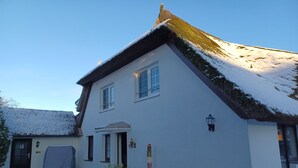 Une maison à deux étages, dont le toit est recouvert de neige, avec une porte d’entrée et un petit porche.