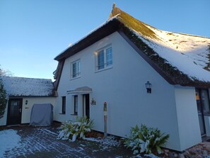 A two-story house with a snow-covered roof, a front door, and a small porch area.