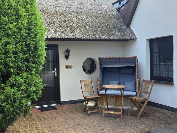 A thatched-roof building with a black door, a small round table with chairs, and a blue cushioned bench.