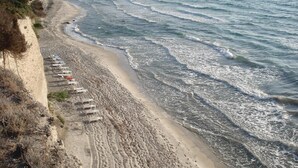Une plage bordée de rangées de transats et de parasols, un rivage sablonneux et des vagues qui déferlent sur la plage.