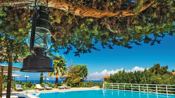Une piscine d’un bleu éclatant, bordée de chaises longues et d’ombrelles, entourée de verdure et offrant une vue sur l’océan.