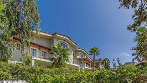 Un immeuble à plusieurs étages doté de balcons, entouré d’une végétation luxuriante.