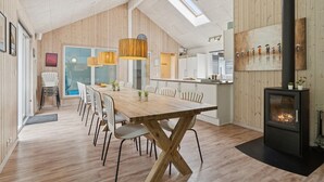 Un comedor amplio con una larga mesa de madera y sillas, una cocina moderna con armarios blancos y una chimenea grande.