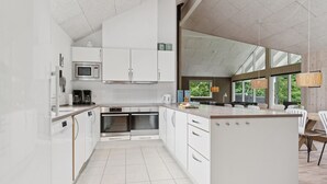 Una cocina moderna con armarios blancos, una isla central y un comedor con luz natural.