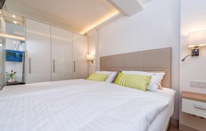 A hotel room with a large bed, a wardrobe, a bedside table, and a wall-mounted TV.