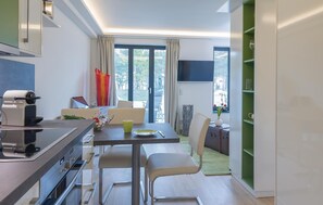 A modern kitchen with a dining area, a TV mounted on the wall, and a view of the outdoors.