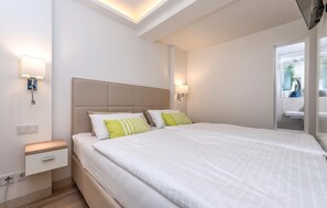 A modern hotel room with a large bed, a nightstand, a wall-mounted lamp, and a ceiling light.