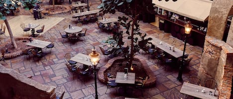Une cour intérieure abritant de nombreuses tables et chaises, entourée de murs en briques et dotée d’un sol en pierre.