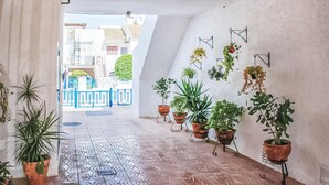 A hallway with patterned floor tiles, potted plants on stands, and a view of a blue balcony and buildings outside. - Amazing apartment in Torrevieja with WiFi (Torrevieja)