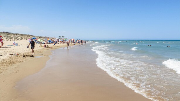 A sandy beach with people walking and swimming, a wooden pier, and umbrellas. - Amazing apartment in Torrevieja with WiFi (Torrevieja)