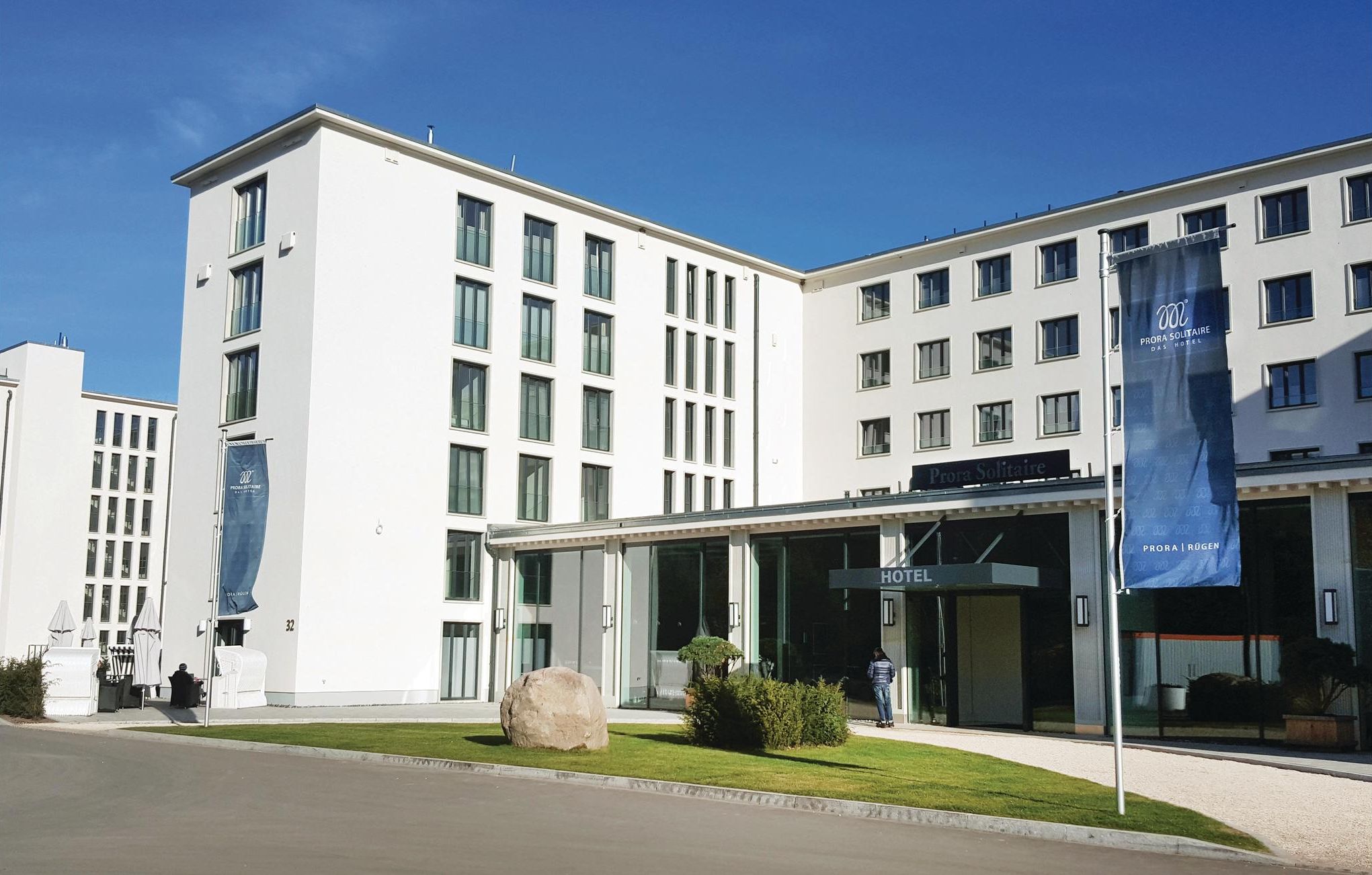 A modern hotel with a glass facade, a prominent entrance, and a large rock in the front garden.