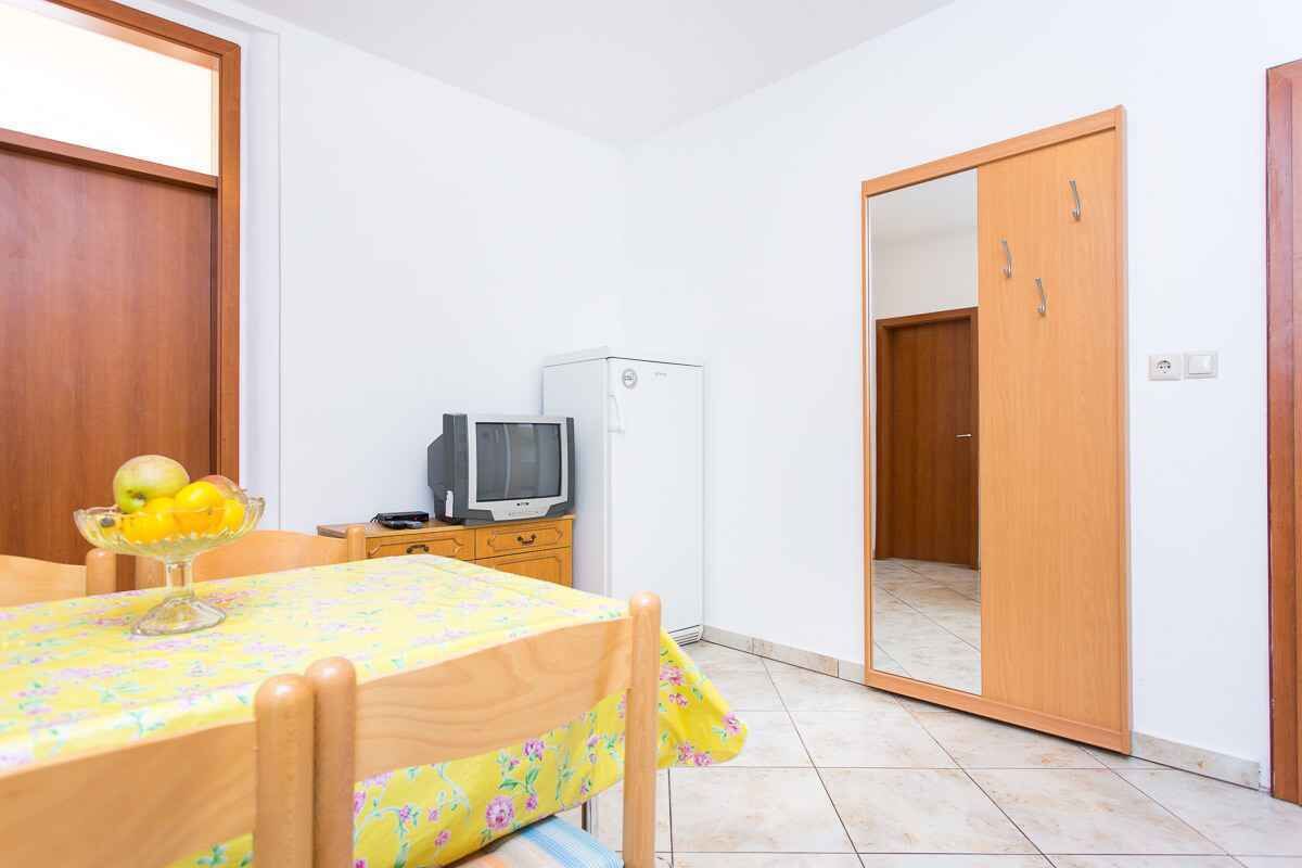 Ein kleiner, ordentlicher Raum mit einem Holztisch, einem Fernseher und einem Kühlschrank.