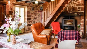 A rustic interior with a stone wall, wooden staircase, leather armchair, dining table with plates and wine glasses, and a fireplace. - Gorgeous home in Badefols D'Ans (Badefols D'Ans)
