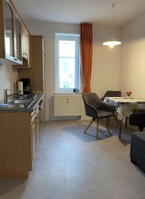 A kitchen with a stove, sink, and window with curtains. There is a dining area with a table and chairs.