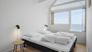 A bedroom with a bed, a small table, two wall-mounted lamps, and a window with a view of the sea. - 3 bedroom gorgeous home in Assens (Assens)