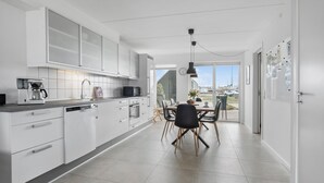 A modern kitchen with white cabinets, a coffee machine, and a dining area with a table and chairs. - 3 bedroom gorgeous home in Assens (Assens)