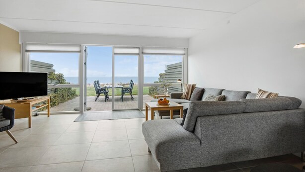 A modern living room with a grey sofa, a flat-screen TV, and a dining area with a table and chairs. - 3 bedroom gorgeous home in Assens (Assens)