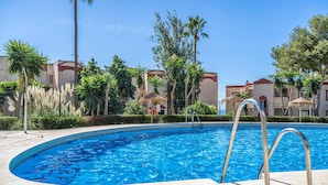A swimming pool with a curved edge, surrounded by palm trees and a fence.