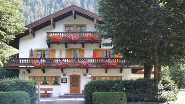 A two-story building with a balcony, wooden shutters, and a bench in front.