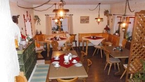 A restaurant with multiple wooden tables and chairs, some with red tablecloths.