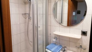 A bathroom with a glass-enclosed shower, a round mirror, and a sink with a towel.
