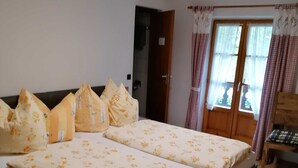 A bedroom with a large bed, a wooden headboard, a door, and a window with curtains.