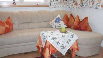 A living room with a sofa, a small table with a floral tablecloth, and a candle.