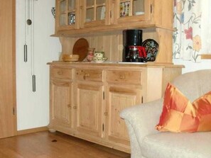 A kitchen with wooden cabinets, a coffee maker, and a floral-patterned curtain. - Ferienalm, Germany (Ruhpolding)