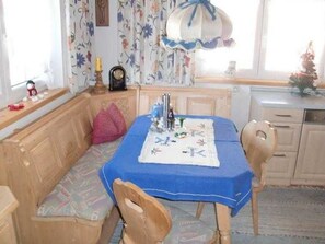 Un comedor con una mesa cubierta por un mantel azul, un banco con un cojín estampado y un reloj colgado en la pared.