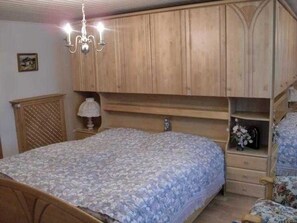 A bedroom with a wooden bed frame, a chandelier, and built-in wooden cabinets. - Ferienalm, Germany (Ruhpolding)