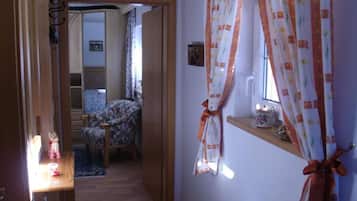 Un pasillo con una puerta de madera, una silla, una mesita con una lámpara y una ventana con cortinas.