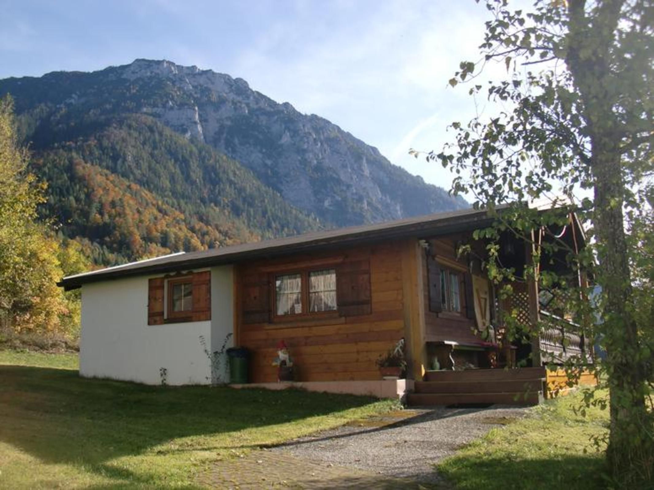 A wooden cabin with a porch, a small garden, and a mountain backdrop.
