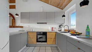 Ett modernt kök med grå skåp, en bänkskiva i trä, en inbyggd ugn och ett fönster som släpper in naturligt ljus.