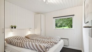 Ein Schlafzimmer mit einem Bett, einem Fenster mit Blick auf Bäume, einem Regal mit Pflanzen und einer Heizung.