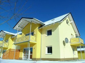 Un edificio amarillo de varios pisos con balcones, una antena parabólica y una entrada con portones.