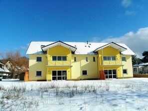 A two-story yellow building with a white roof, multiple windows, and a flat front.