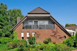 A two-story house with a brick exterior, a balcony on the upper floor, and a chimney.