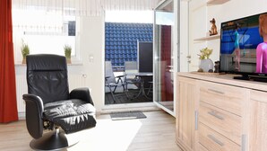 Ein modernes Wohnzimmer mit einem Ledersessel, einem Fernseher und einer Glastür, die zu einem Außenbereich mit blau gefliestem Dach führt.