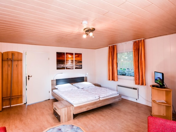 A bedroom with a bed, a wardrobe, a window with curtains, a radiator, and a TV on a wooden stand.
