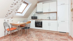 A kitchen with white cabinets, a microwave, an oven, and a dining area with two chairs and a table.