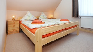 A single wooden bed with orange bedding, two bedside tables with lamps, and a window with curtains.