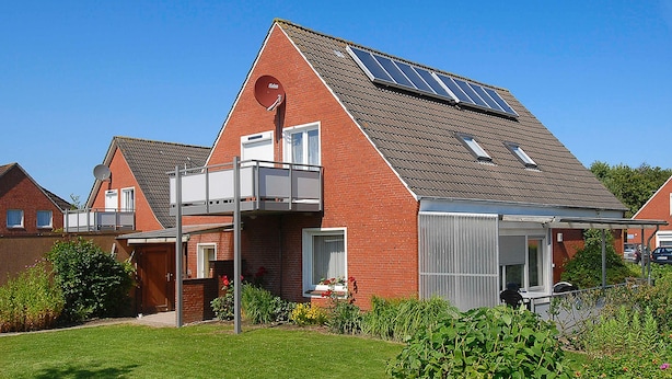 A modern house with a sloped roof, solar panels, a satellite dish, and a small balcony.