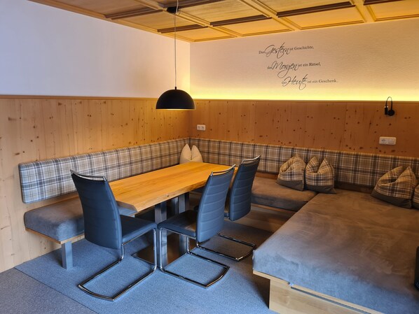 Una habitación acogedora con un banco de madera, una mesa y sillas. En una pared, hay una cita en alemán.
