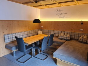 A cozy room with a wooden bench, a table, and chairs. There is a wall with a quote in German.