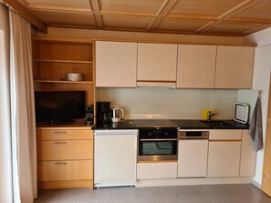 A compact kitchen with wooden cabinets, a dishwasher, an oven, a coffee maker, and a television. - Vacation apartment 1 - Üntschenblick - Guesthouse Monika (Au)