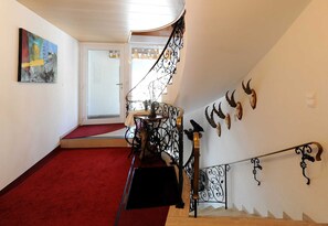 A staircase with ornate metal railings, a red carpeted floor, and decorative wall art. - Vacation apartment 1 - Üntschenblick - Guesthouse Monika (Au)