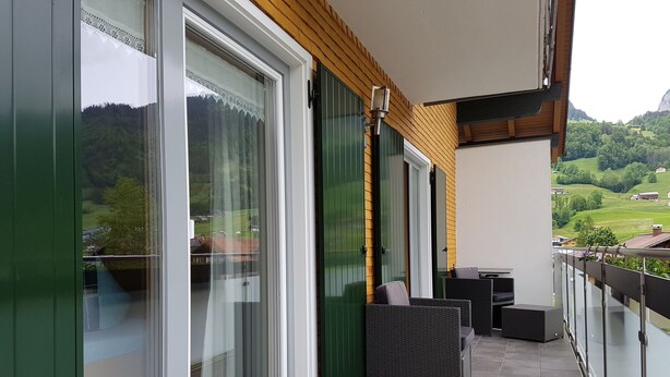 Un balcón con puertas correderas de vidrio, mobiliario exterior y vistas a un paisaje verde.