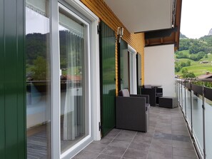 A balcony with sliding glass doors, outdoor furniture, and a view of a green landscape.